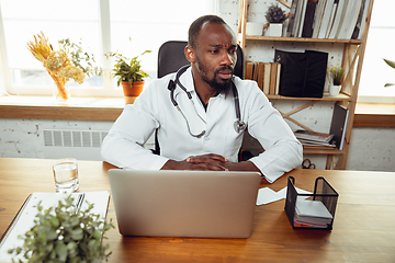 Image showing African-american doctor consulting for patient, working in cabinet