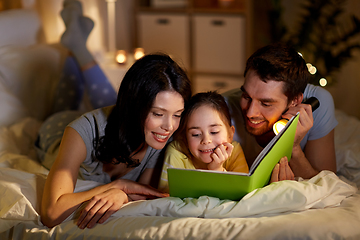 Image showing happy family reading book in bed at night at home