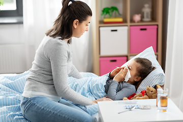 Image showing mother and ill little daughter blowing nose in bed