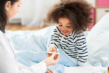 Image showing doctor showing thermometer to smiling sick girl