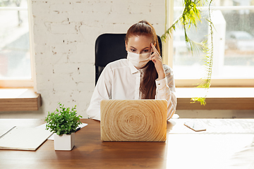 Image showing Woman working in office alone during coronavirus or COVID-19 quarantine, wearing face mask