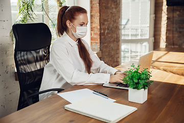 Image showing Woman working in office alone during coronavirus or COVID-19 quarantine, wearing face mask