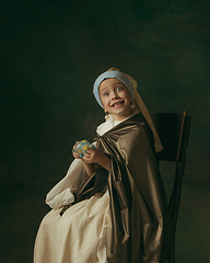 Image showing Medieval little girl as a lady with a pearl earring on dark studio background. Concept of comparison of eras, childhood. Stylish creative design, art vision, new look of artwork.