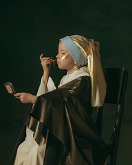 Image showing Medieval little girl as a lady with a pearl earring on dark studio background. Concept of comparison of eras, childhood. Stylish creative design, art vision, new look of artwork.