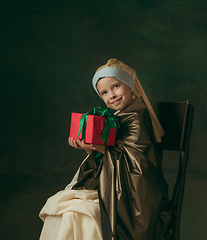 Image showing Medieval little girl as a lady with a pearl earring on dark studio background. Concept of comparison of eras, childhood. Stylish creative design, art vision, new look of artwork.