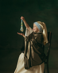 Image showing Medieval little girl as a lady with a pearl earring on dark studio background. Concept of comparison of eras, childhood. Stylish creative design, art vision, new look of artwork.