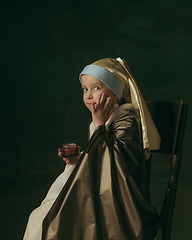 Image showing Medieval little girl as a lady with a pearl earring on dark studio background. Concept of comparison of eras, childhood. Stylish creative design, art vision, new look of artwork.