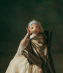 Image showing Medieval little girl as a lady with a pearl earring on dark studio background. Concept of comparison of eras, childhood. Stylish creative design, art vision, new look of artwork.