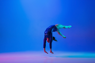 Image showing Young flexible girl isolated on blue studio background. Young female model practicing artistic gymnastics. Exercises for flexibility, balance.