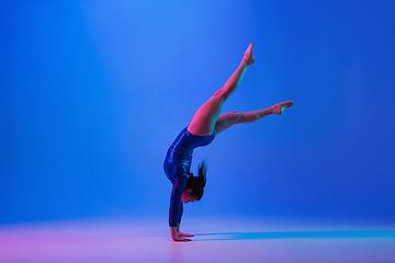 Image showing Young flexible girl isolated on blue studio background. Young female model practicing artistic gymnastics. Exercises for flexibility, balance.