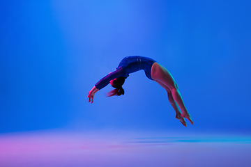 Image showing Young flexible girl isolated on blue studio background. Young female model practicing artistic gymnastics. Exercises for flexibility, balance.