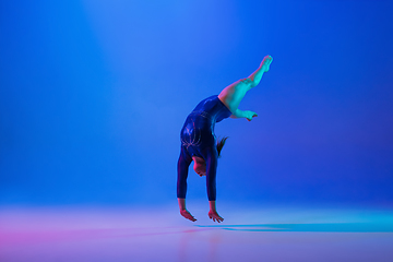 Image showing Young flexible girl isolated on blue studio background. Young female model practicing artistic gymnastics. Exercises for flexibility, balance.