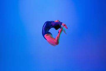 Image showing Young flexible girl isolated on blue studio background. Young female model practicing artistic gymnastics. Exercises for flexibility, balance.