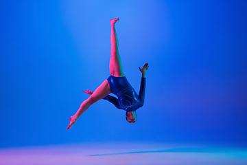 Image showing Young flexible girl isolated on blue studio background. Young female model practicing artistic gymnastics. Exercises for flexibility, balance.