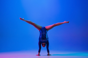 Image showing Young flexible girl isolated on blue studio background. Young female model practicing artistic gymnastics. Exercises for flexibility, balance.