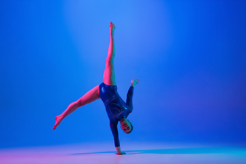 Image showing Young flexible girl isolated on blue studio background. Young female model practicing artistic gymnastics. Exercises for flexibility, balance.