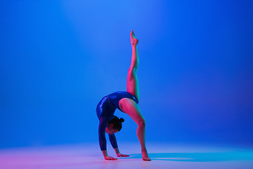 Image showing Young flexible girl isolated on blue studio background. Young female model practicing artistic gymnastics. Exercises for flexibility, balance.