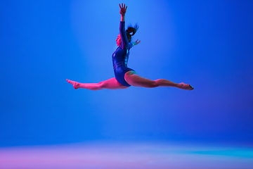 Image showing Young flexible girl isolated on blue studio background. Young female model practicing artistic gymnastics. Exercises for flexibility, balance.