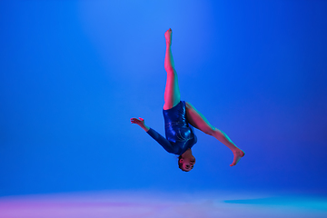 Image showing Young flexible girl isolated on blue studio background. Young female model practicing artistic gymnastics. Exercises for flexibility, balance.