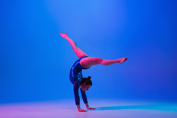 Image showing Young flexible girl isolated on blue studio background. Young female model practicing artistic gymnastics. Exercises for flexibility, balance.