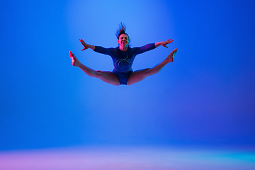 Image showing Young flexible girl isolated on blue studio background. Young female model practicing artistic gymnastics. Exercises for flexibility, balance.