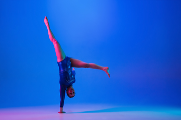 Image showing Young flexible girl isolated on blue studio background. Young female model practicing artistic gymnastics. Exercises for flexibility, balance.