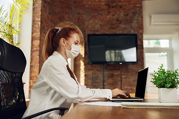 Image showing Woman working in office alone during coronavirus or COVID-19 quarantine, wearing face mask