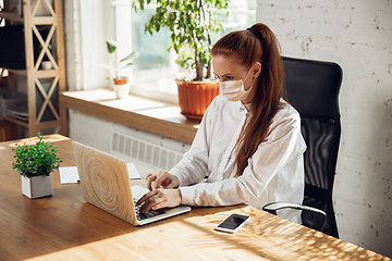 Image showing Woman working in office alone during coronavirus or COVID-19 quarantine, wearing face mask