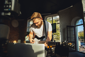 Image showing Caucasian musician playing guitar during online concert at home isolated and quarantined, impressive improvising in sunlight