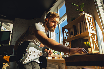 Image showing Caucasian musician playing guitar during online concert at home isolated and quarantined, tuning the stream
