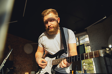 Image showing Caucasian musician playing guitar during online concert at home isolated and quarantined, impressive improvising in sunlight