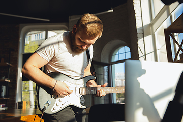 Image showing Caucasian musician playing guitar during online concert at home isolated and quarantined, impressive improvising in sunlight