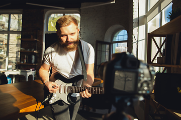 Image showing Caucasian musician playing guitar during online concert at home isolated and quarantined, impressive improvising in sunlight