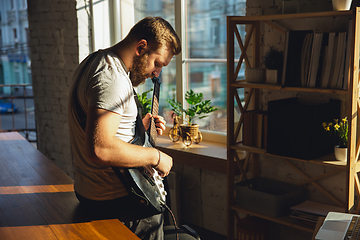 Image showing Caucasian musician playing guitar during online concert at home isolated and quarantined, impressive improvising in sunlight