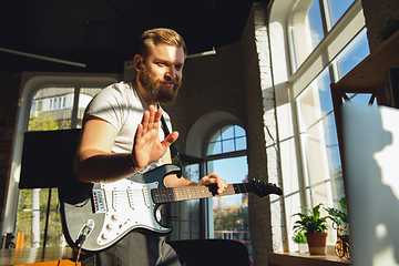 Image showing Caucasian musician playing guitar during online concert at home isolated and quarantined, greeting