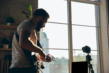 Image showing Caucasian musician playing guitar during online concert at home isolated and quarantined, impressive improvising