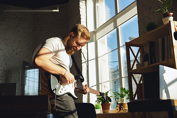 Image showing Caucasian musician playing guitar during online concert at home isolated and quarantined, impressive improvising in sunlight