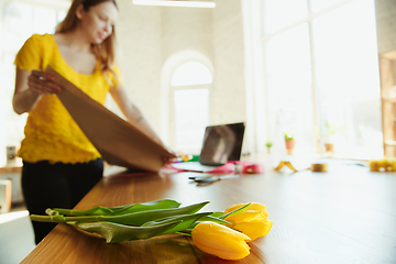 Image showing Florist at work: woman shows how to make bouquet with tulips, working at home concept, using coverage paper