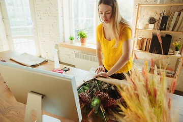 Image showing Florist at work: woman shows how to make bouquet, working at home concept, using paper coverage