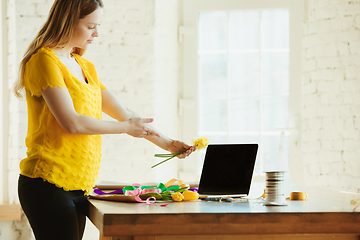 Image showing Florist at work: woman shows how to make bouquet with tulips, working at home concept, adds daffodils