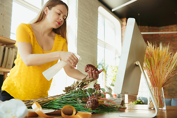 Image showing Florist at work: woman shows how to make bouquet, working at home concept, spraying