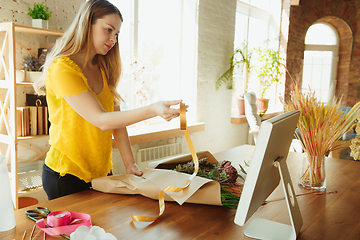 Image showing Florist at work: woman shows how to make bouquet, working at home concept, using paper coverage