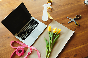 Image showing Florist at work: table with tulips and daffodils, ribbons and coverage paper against laptop, prepared for workshop