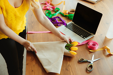 Image showing Florist at work: woman shows how to make bouquet with tulips, working at home concept, using coverage paper