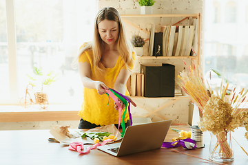 Image showing Florist at work: woman shows how to make bouquet with tulips, working at home concept, choosing decoration