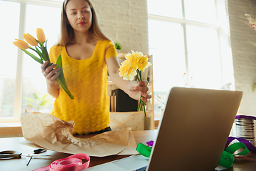 Image showing Florist at work: woman shows how to make bouquet with tulips, working at home concept, choosing flowers