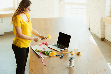 Image showing Florist at work: woman shows how to make bouquet with tulips, working at home concept, adds daffodils