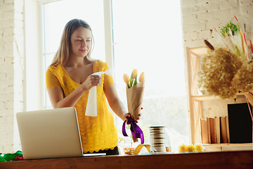 Image showing Florist at work: woman shows how to make bouquet with tulips, working at home concept, using spray