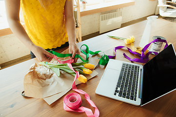 Image showing Florist at work: woman shows how to make bouquet with tulips, working at home concept, choosing decoration