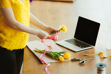 Image showing Florist at work: woman shows how to make bouquet with tulips, working at home concept, adds daffodils